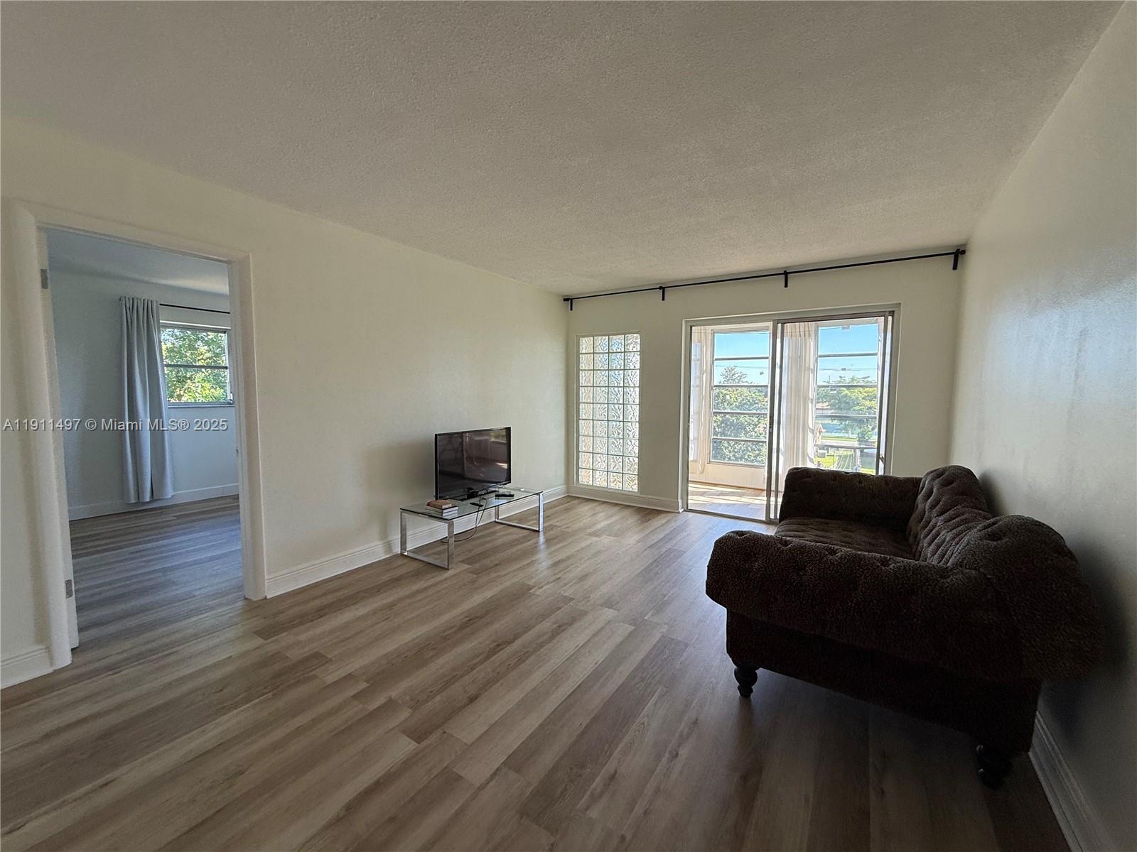 A living room features light wood-look flooring, a dark sofa, and a glass sliding door — 4310 NW 12th Ct # 302, Lauderhill FL 33313, LAUDERHILL, FL