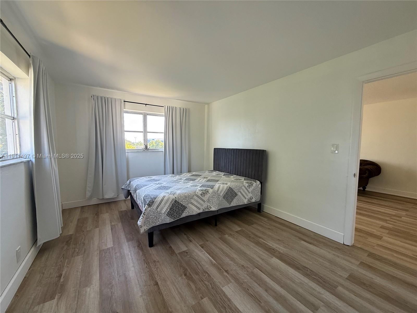 A bedroom features a gray upholstered bed, light wood-look flooring, and white walls — 4310 NW 12th Ct # 302, Lauderhill FL 33313, LAUDERHILL, FL