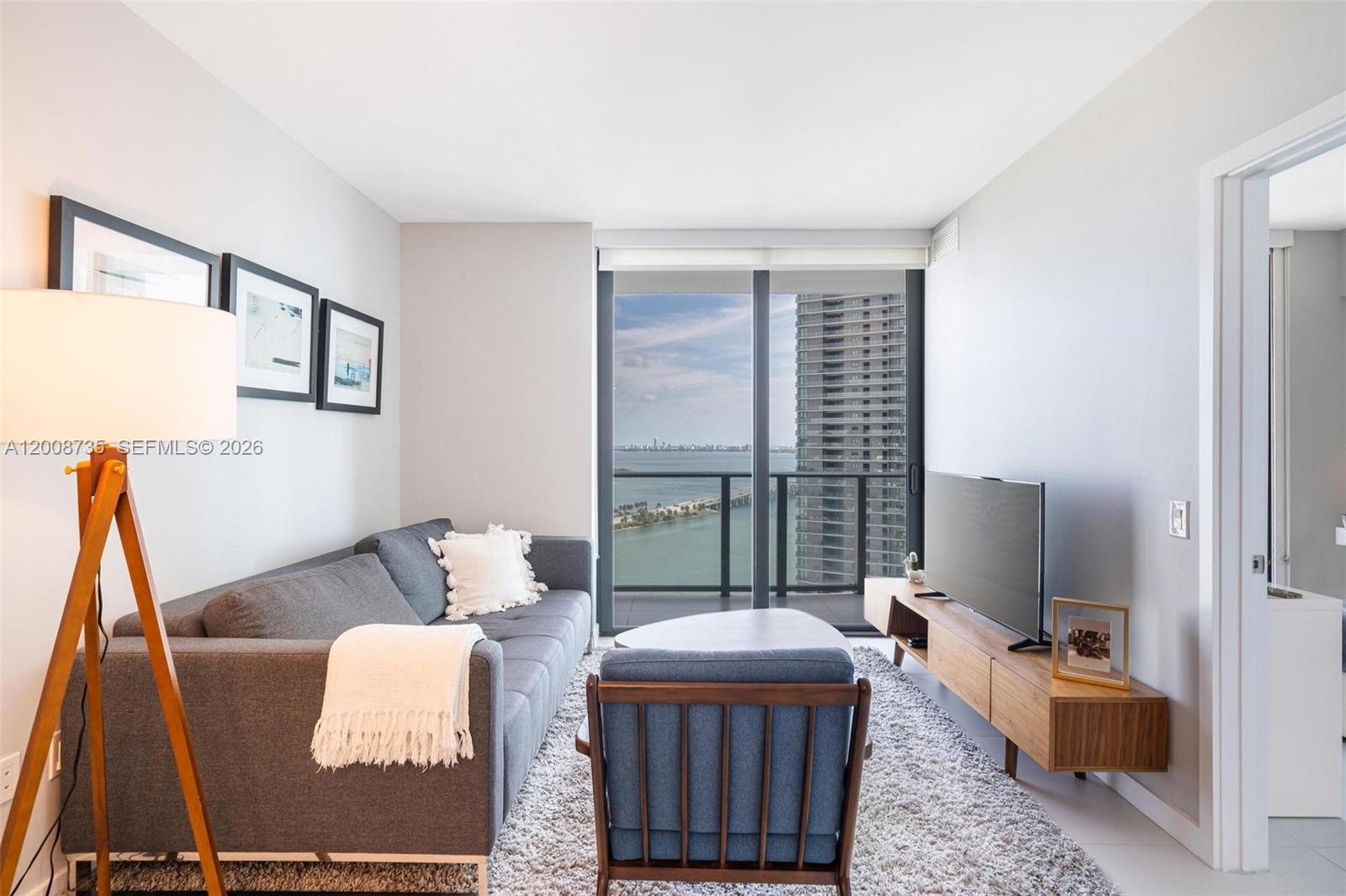 A living room features a grey sofa, blue armchair, media console, and a balcony view — 501 NE 31st St # 2703, Miami FL 33137, MIAMI, FL