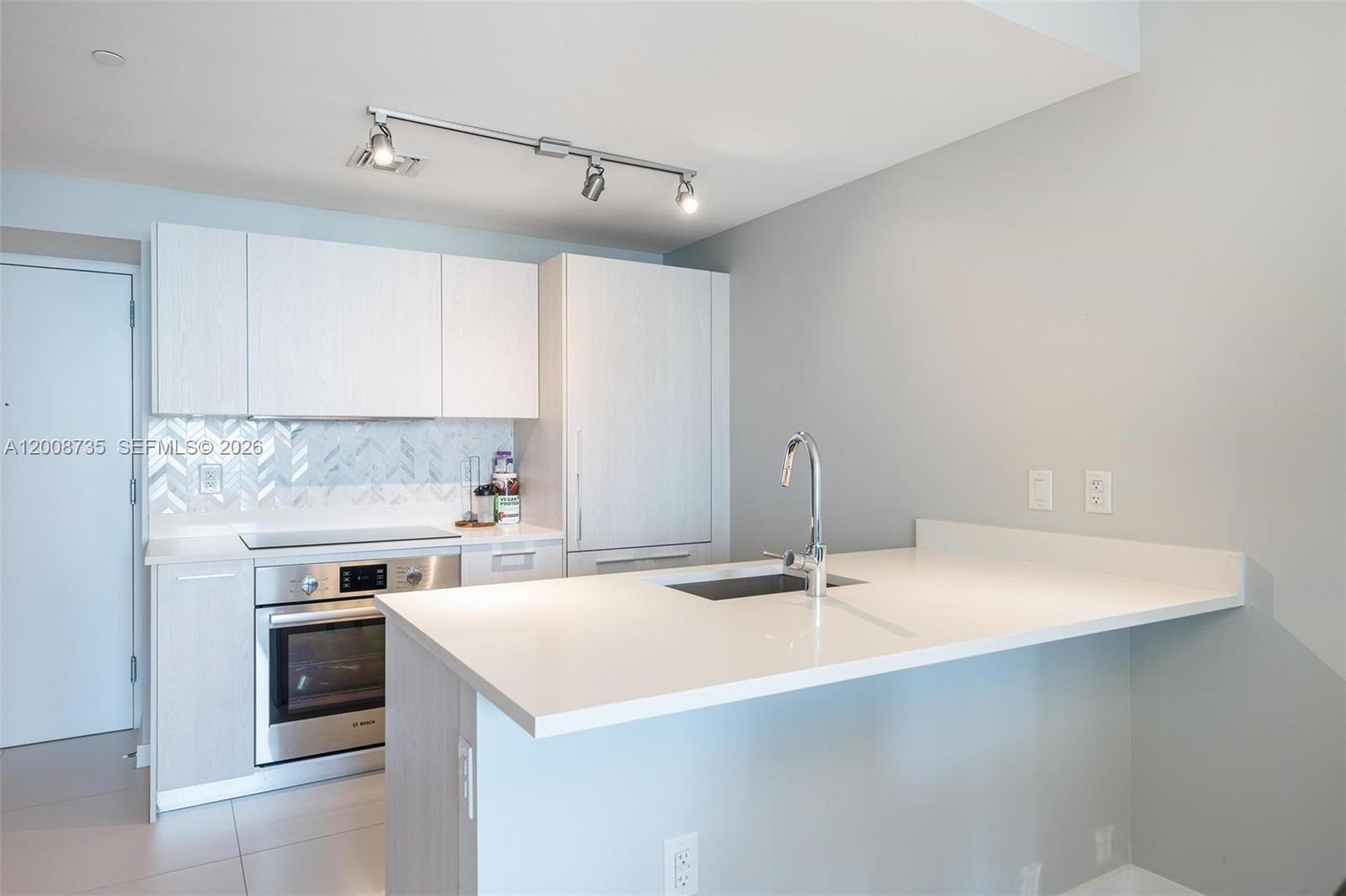 A modern kitchen features white cabinetry, stainless steel appliances, and a white quartz peninsula — 501 NE 31st St # 2703, Miami FL 33137, MIAMI, FL