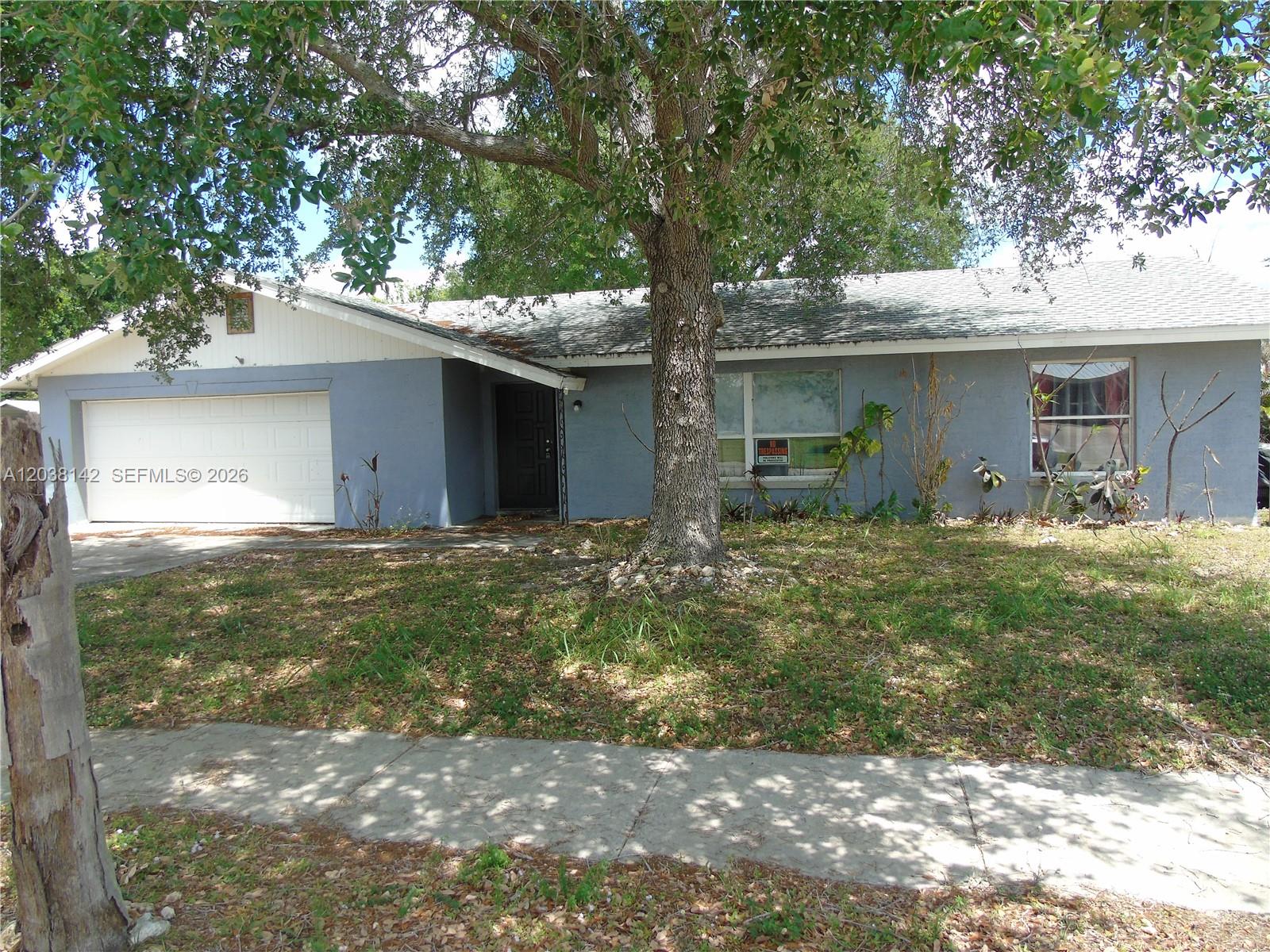 A single-story gray house features a white garage door and a large tree out front — 1549 lime dr, Melbourne FL 32935, MELBOURNE, FL