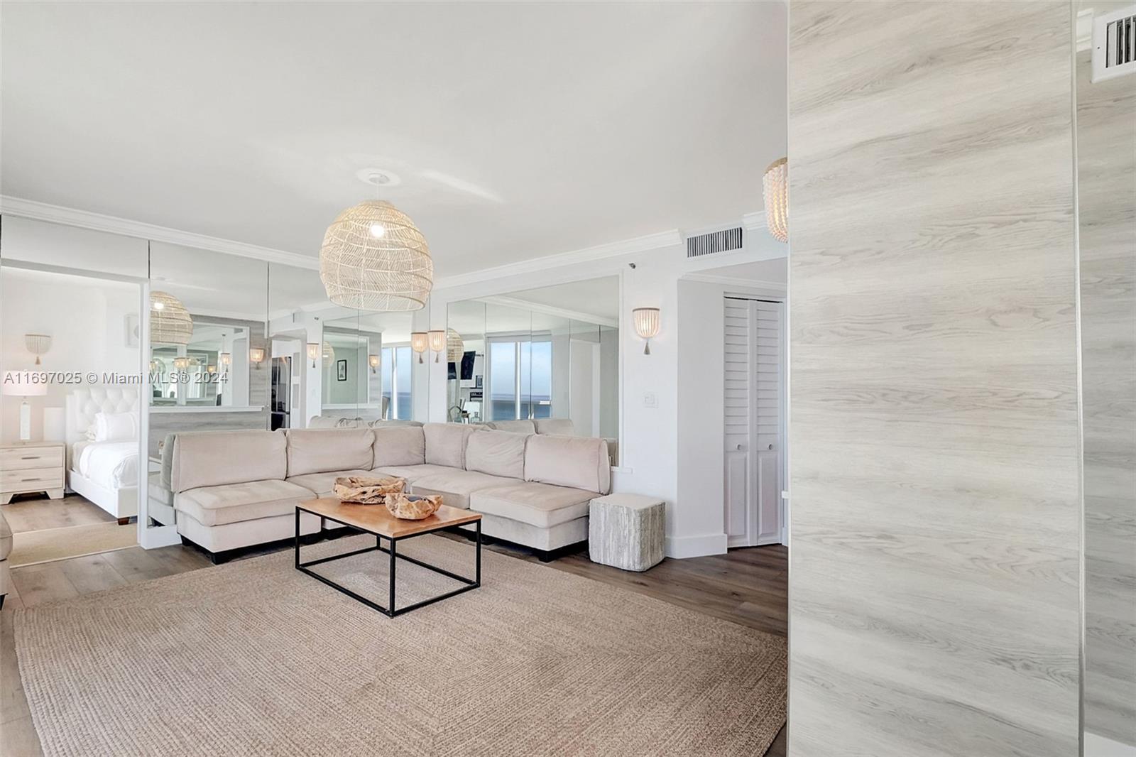 A living room features a large beige sectional sofa, a coffee table, and mirrored walls — 2401 Collins Ave # 1902, Miami Beach FL 33140, MIAMI BEACH, FL