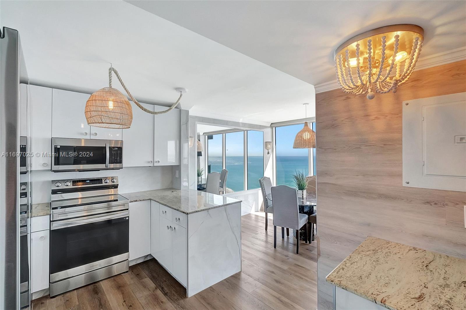A modern kitchen with white cabinets, marble-look counters, and a dining area overlooking the ocean — 2401 Collins Ave # 1902, Miami Beach FL 33140, MIAMI BEACH, FL