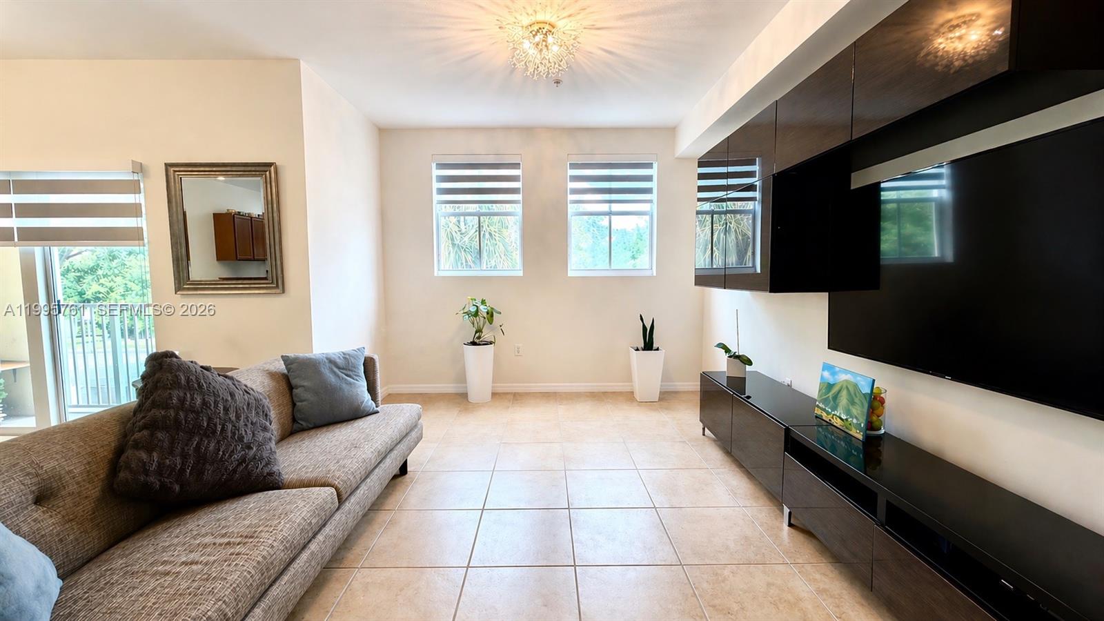 A living room features a sofa, a wall-mounted television, and tile flooring — 10870 NW 88th Ter # 216, Doral FL 33178, DORAL, FL