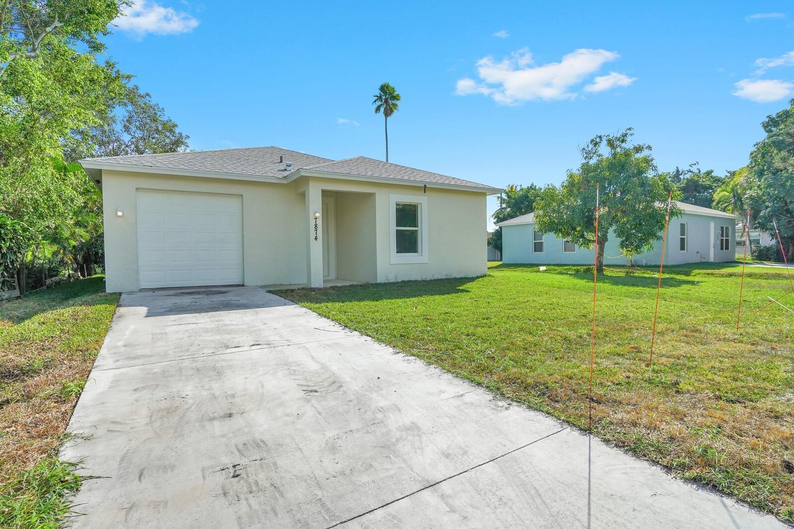 A light-colored single-story house with a concrete driveway and a garage under a blue sky — 7874 Griswold Street, Lantana FL 33462, LANTANA, FL