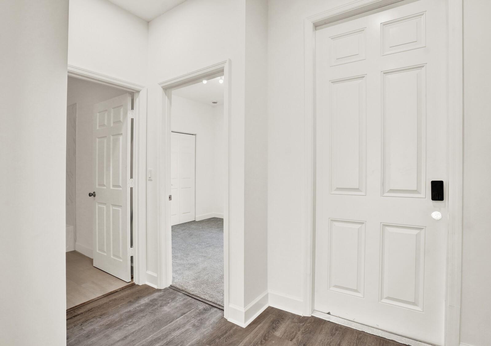 A hallway with wood-look flooring leads to a carpeted bedroom and a tiled bathroom — 7874 Griswold Street, Lantana FL 33462, LANTANA, FL