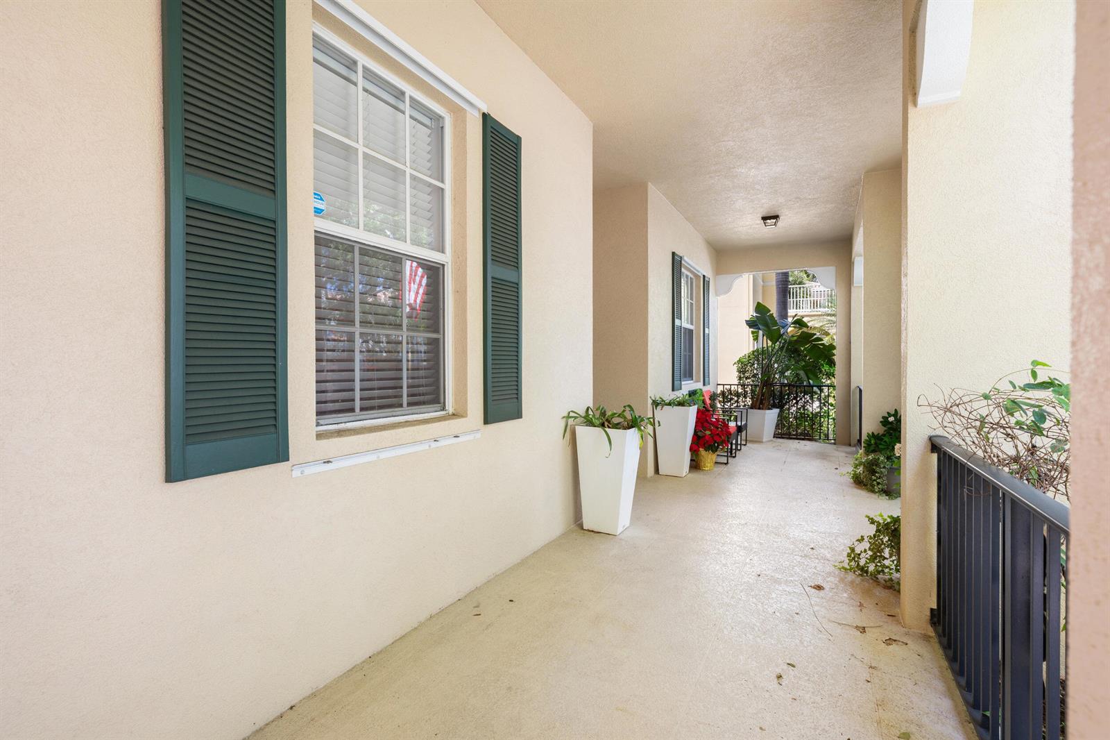 A covered outdoor balcony features beige stucco walls, green shutters, and several potted plants — 310 San Remo Drive, Jupiter FL 33458, JUPITER, FL