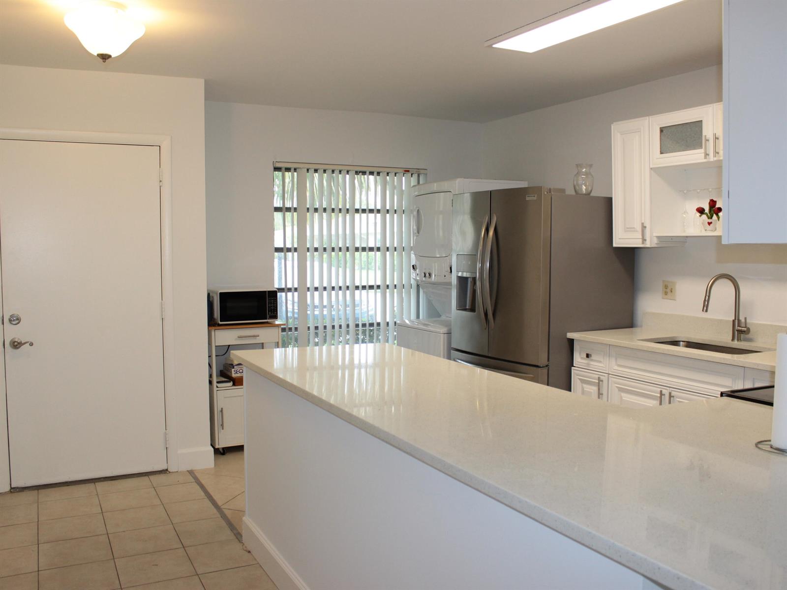 A kitchen features white cabinetry, a quartz countertop island, stainless steel appliances, and tile flooring — 8573 Boca Drive # 3, Boca Raton FL 33433, BOCA RATON, FL