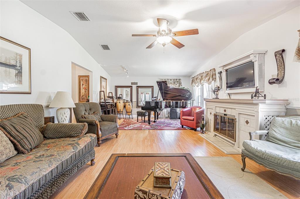 A living room features a grand piano, a fireplace, hardwood floors, and various seating areas — 37627 LORENA AVENUE, ZEPHYRHILLS, FL