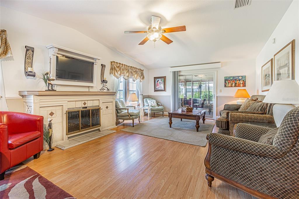 A living room features a fireplace, wood-look flooring, a ceiling fan, and multiple seating areas — 37627 LORENA AVENUE, ZEPHYRHILLS, FL