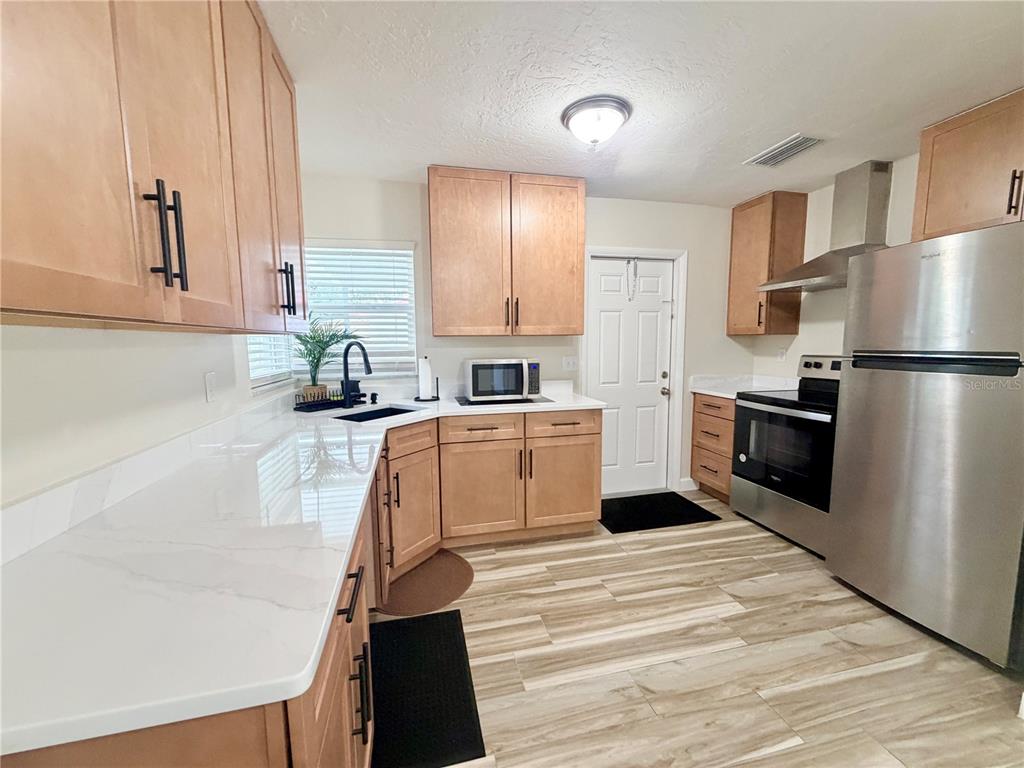 A kitchen features light wood cabinets, white countertops, stainless steel appliances, and wood-look flooring — 1650 HASTINGS DRIVE, DELTONA, FL