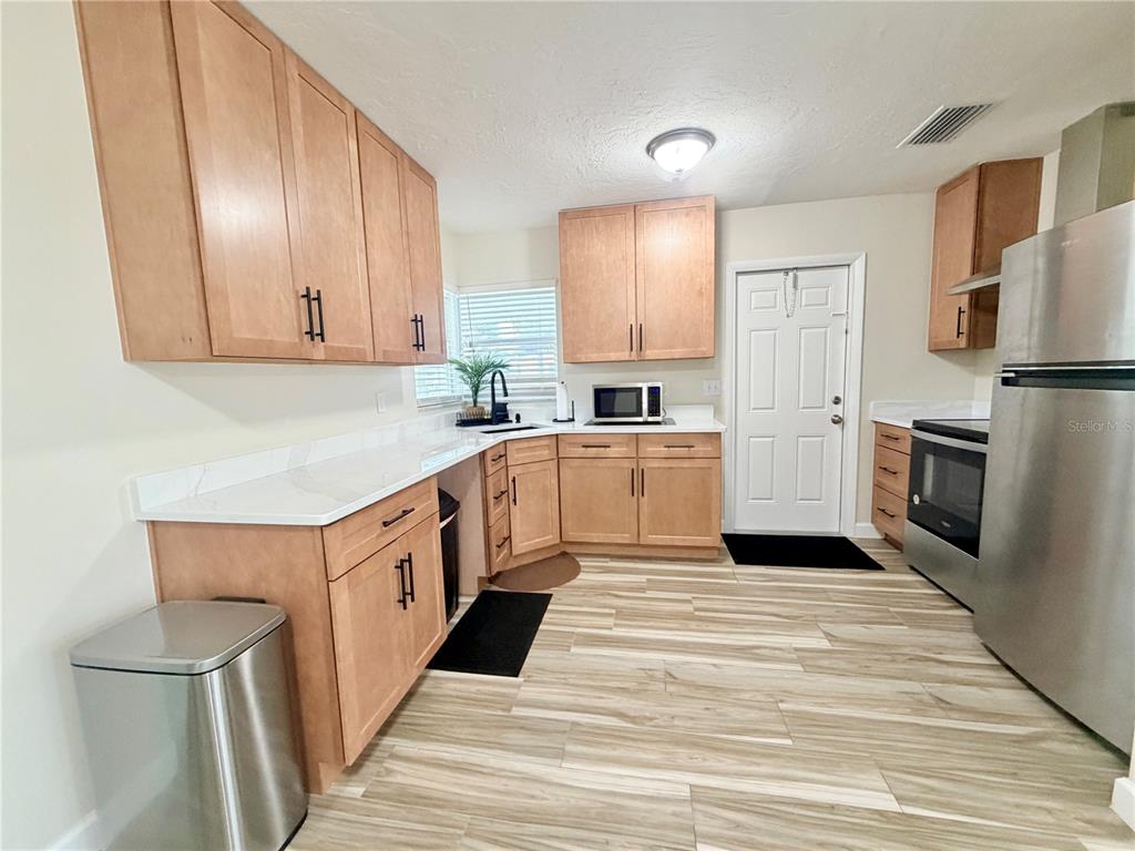 A kitchen features light wood cabinets, white countertops, stainless steel appliances, and wood-look tile flooring — 1650 HASTINGS DRIVE, DELTONA, FL
