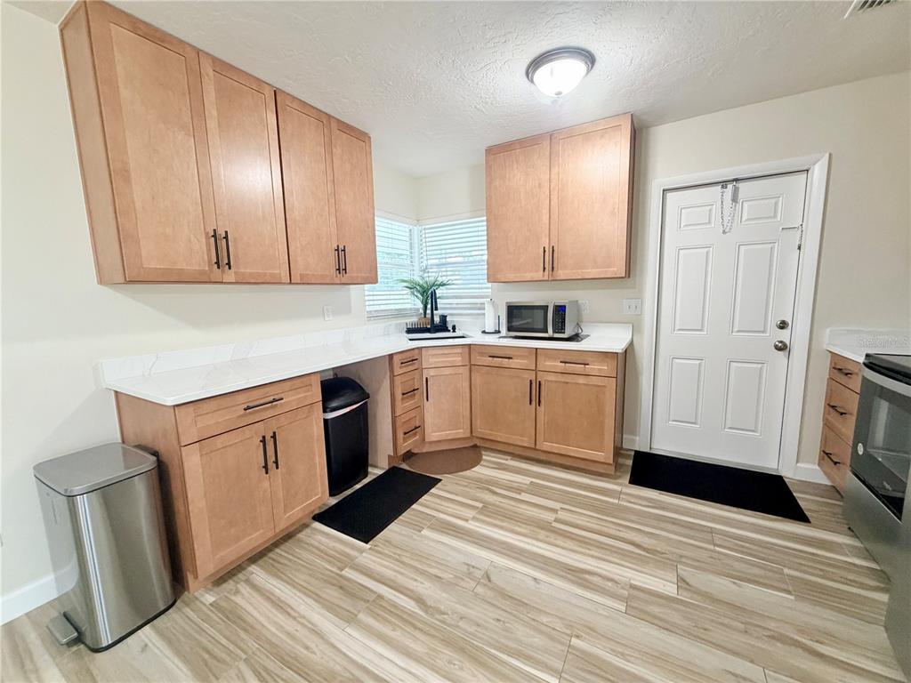 A kitchen features light wood cabinets, white countertops, and wood-look tile flooring — 1650 HASTINGS DRIVE, DELTONA, FL