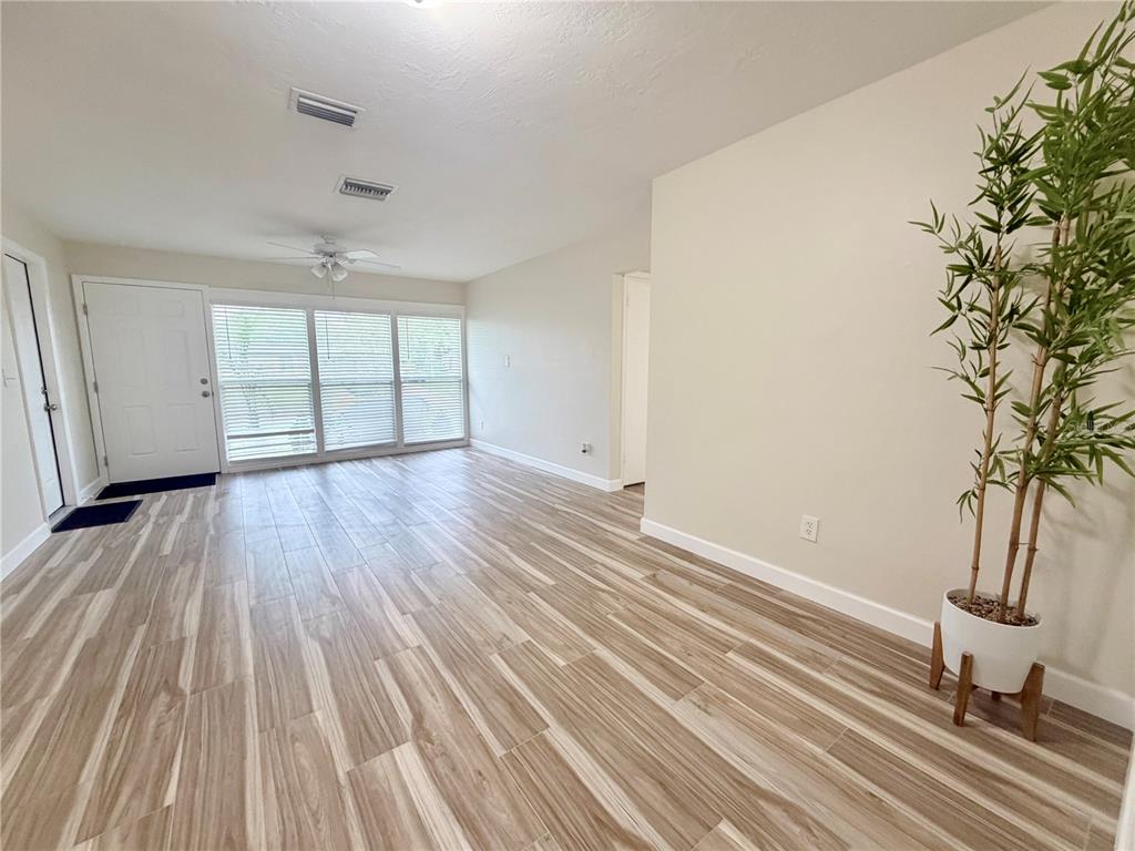An empty living room features wood-look tile flooring, a ceiling fan, and a potted plant — 1650 HASTINGS DRIVE, DELTONA, FL