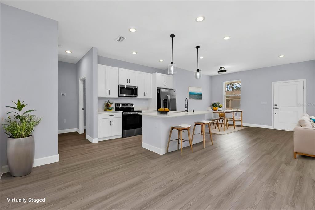 A modern open-concept kitchen features white cabinetry, a central island with bar stools, and flooring — 71 STANHOPE STREET, PORT CHARLOTTE, FL