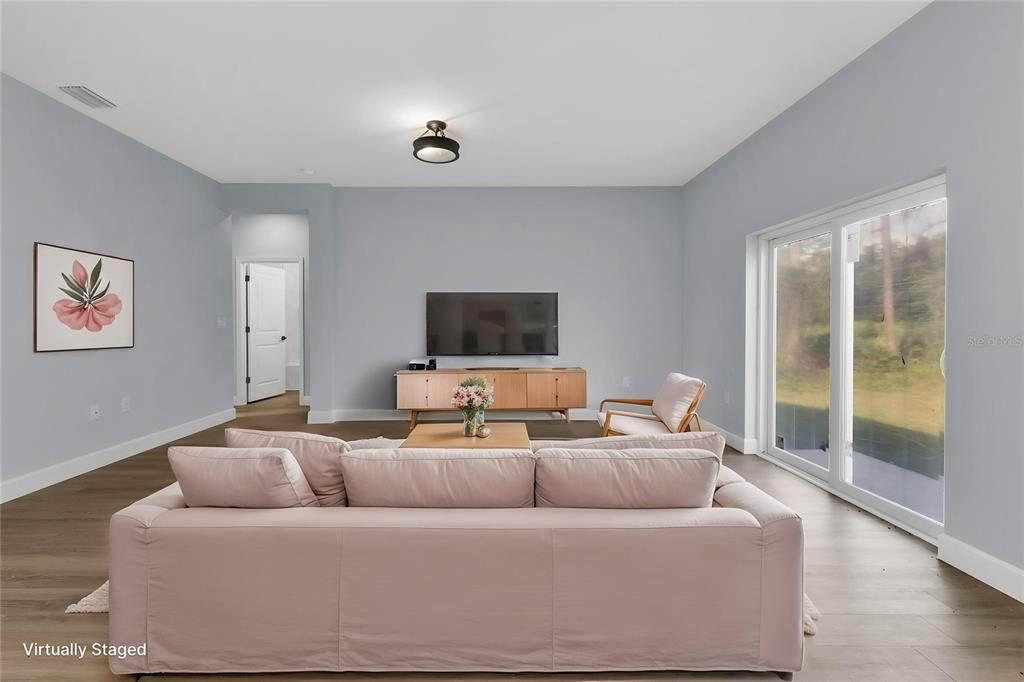This virtually staged living room features light gray walls, wood-look flooring, and a sliding glass door — 71 STANHOPE STREET, PORT CHARLOTTE, FL