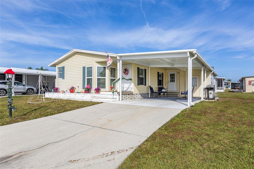 A light yellow manufactured home features a concrete driveway, a carport, and a front porch — 512 LA PLAYA CIRCLE, NORTH PORT, FL