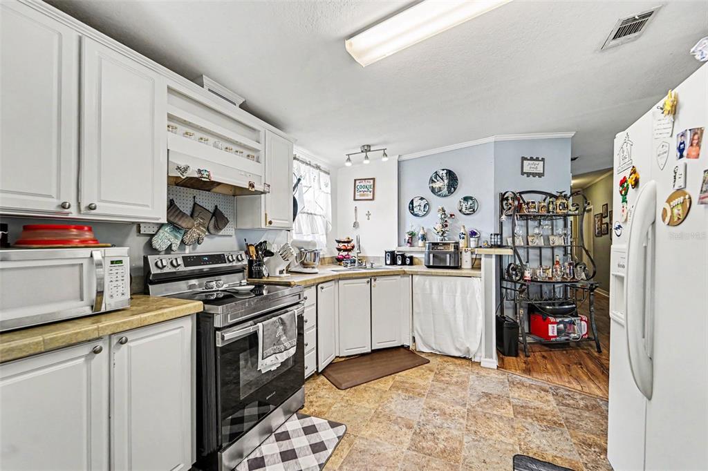 A kitchen features white cabinets, a black stove, tile flooring, and a metal shelving unit — 38030 LAWANDA LOOP, ZEPHYRHILLS, FL