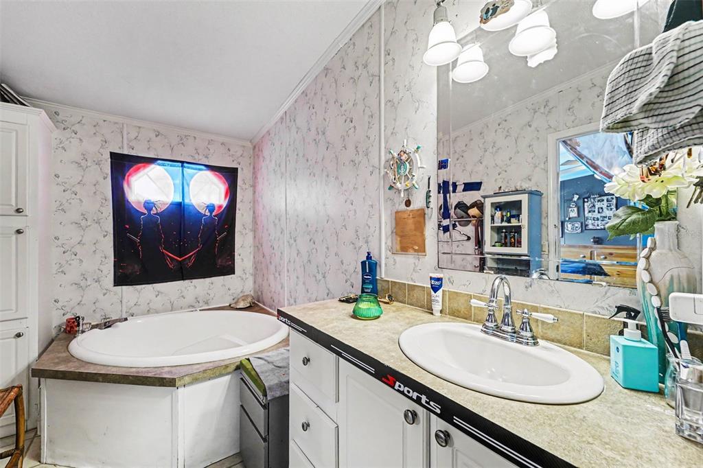A bathroom features a corner soaking tub, a vanity with a sink, and floral wallpaper — 38030 LAWANDA LOOP, ZEPHYRHILLS, FL