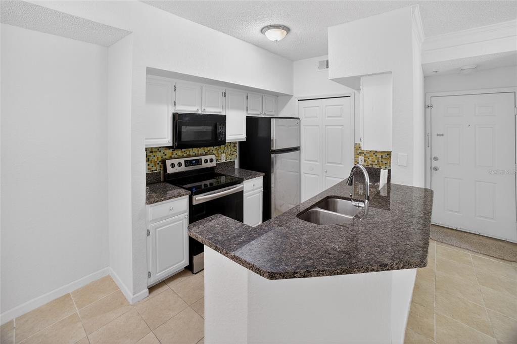 A kitchen features white cabinets, dark granite countertops, black appliances, and a breakfast bar — 13003 PLANTATION PARK CIRCLE UNIT 1323, ORLANDO, FL