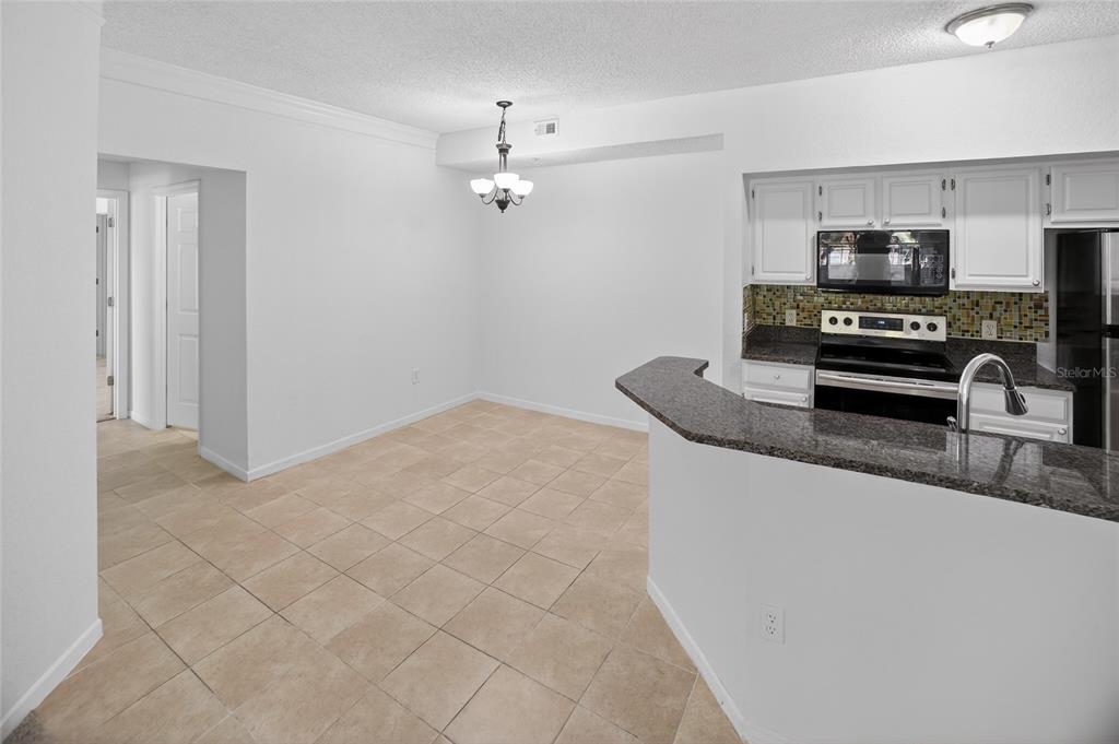 A dining area with tile floors sits adjacent to a kitchen with granite countertops — 13003 PLANTATION PARK CIRCLE UNIT 1323, ORLANDO, FL