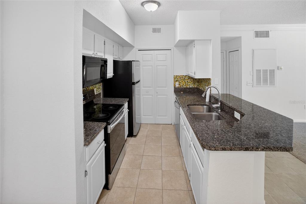 A kitchen features white cabinets, dark granite countertops, black appliances, and a tiled floor — 13003 PLANTATION PARK CIRCLE UNIT 1323, ORLANDO, FL