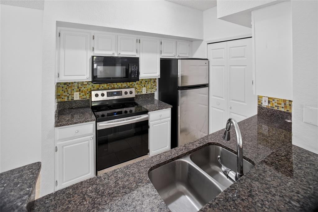 A kitchen features white cabinets, dark granite countertops, stainless steel appliances, and a mosaic backsplash — 13003 PLANTATION PARK CIRCLE UNIT 1323, ORLANDO, FL