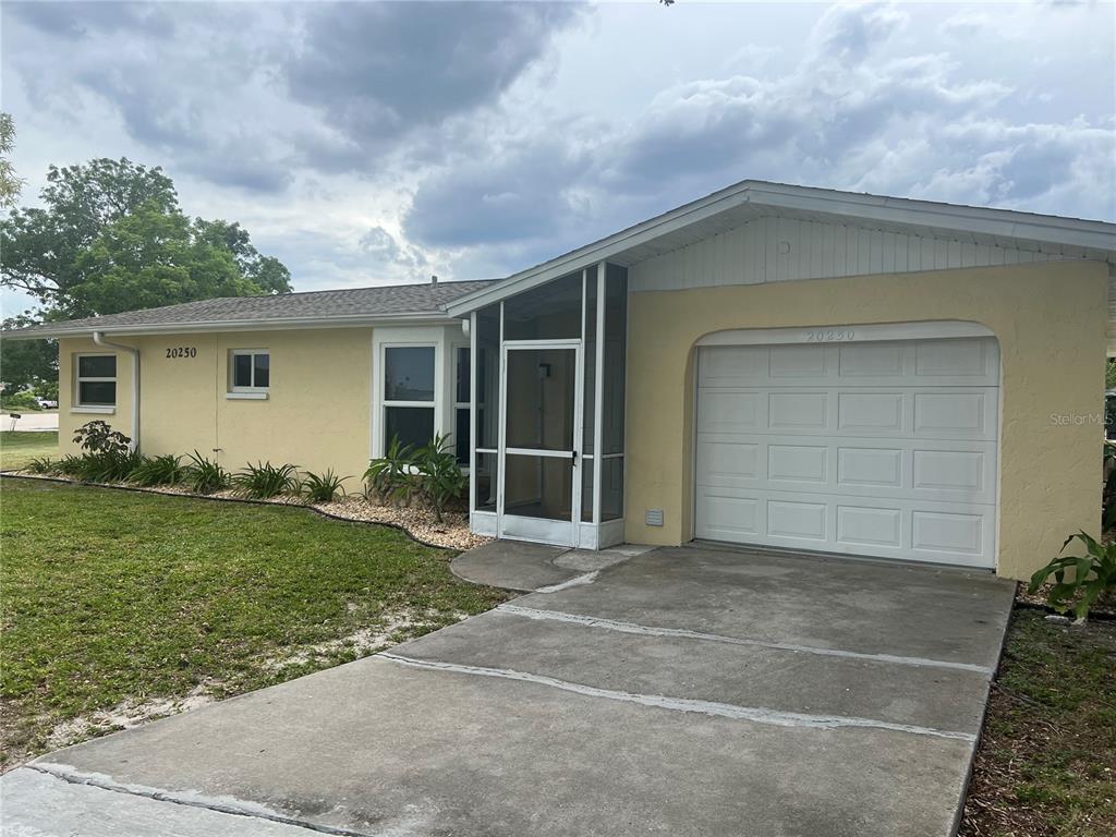 A single-story house with yellow stucco siding, a screened entryway, and a one-car garage — 20250 MIDWAY BOULEVARD, PORT CHARLOTTE, FL