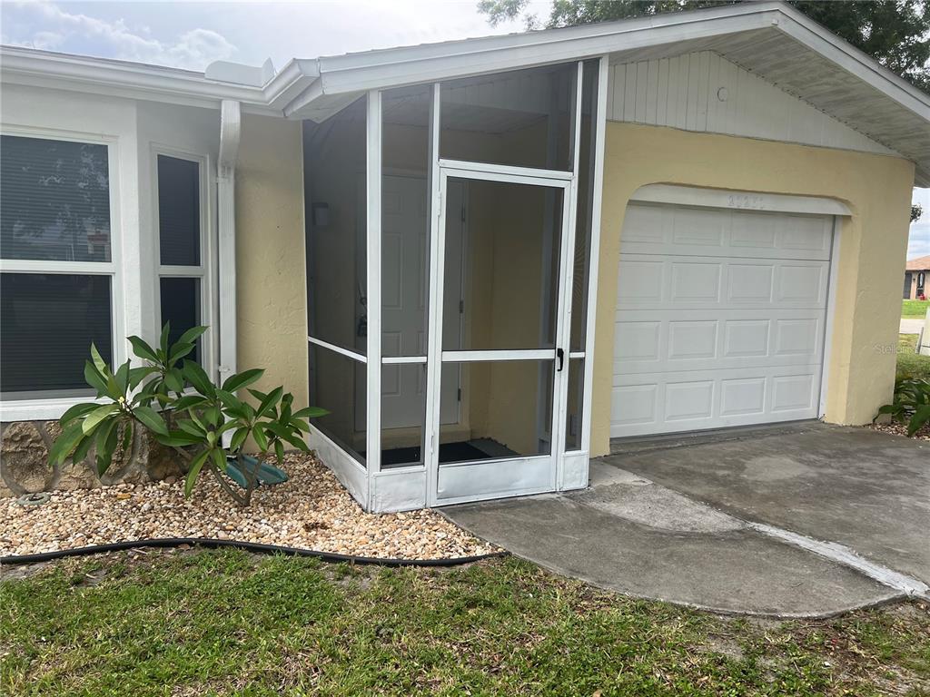 A single-story house exterior features a screened front entryway, a garage, and a landscaped yard — 20250 MIDWAY BOULEVARD, PORT CHARLOTTE, FL