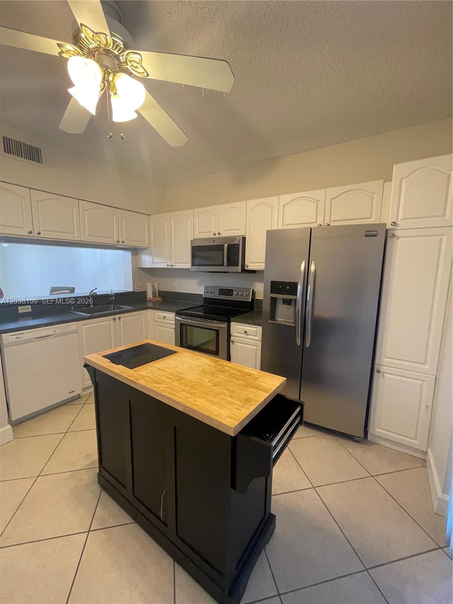 A kitchen features white cabinets, stainless steel appliances, a dark island, and tile flooring — 3100 SW 50th St, Dania Beach FL 33312, DANIA BEACH, FL