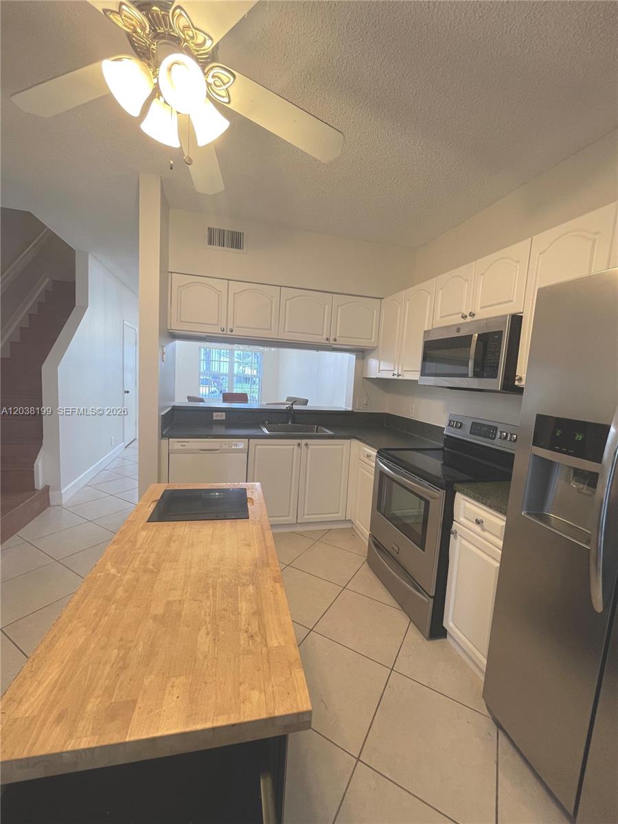 A kitchen features white cabinets, stainless steel appliances, a butcher block island, and tile flooring — 3100 SW 50th St, Dania Beach FL 33312, DANIA BEACH, FL