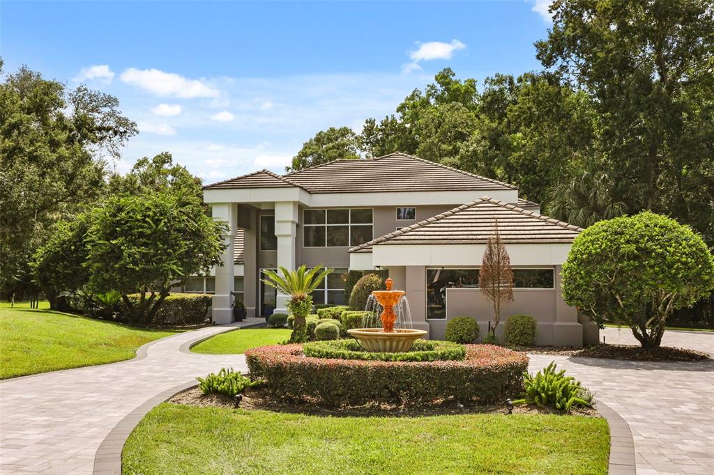 A two-story house with a paved driveway, a central fountain, and surrounding trees — 359 VISTA OAK DRIVE, LONGWOOD, FL