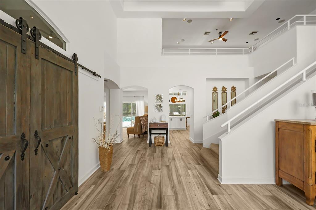 A bright entryway features wood-look flooring, a sliding barn door, and a staircase with railings — 359 VISTA OAK DRIVE, LONGWOOD, FL