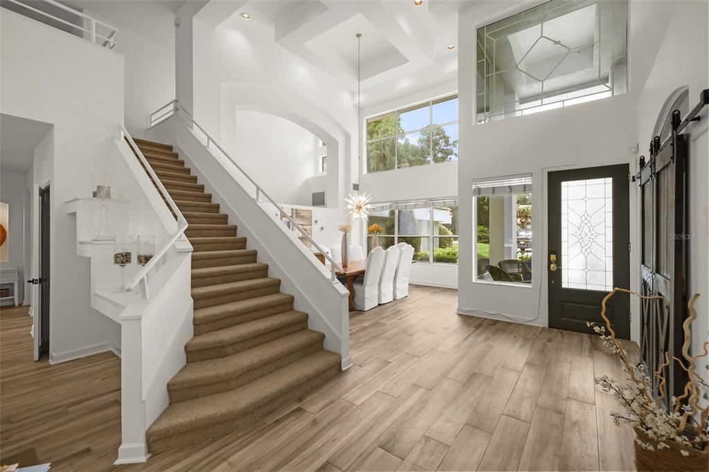 A bright foyer features a carpeted staircase, wood-look tile flooring, and a high vaulted ceiling — 359 VISTA OAK DRIVE, LONGWOOD, FL