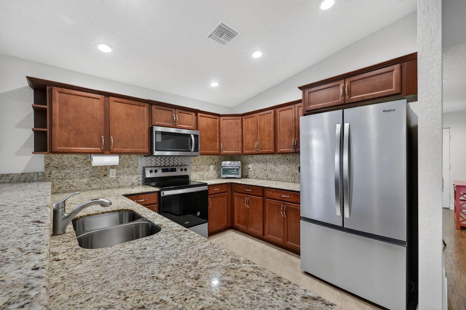 A kitchen features wood cabinets, granite countertops, stainless steel appliances, and a double-basin sink — 6456 Alemendra, Fort Pierce FL 34951, FORT PIERCE, FL
