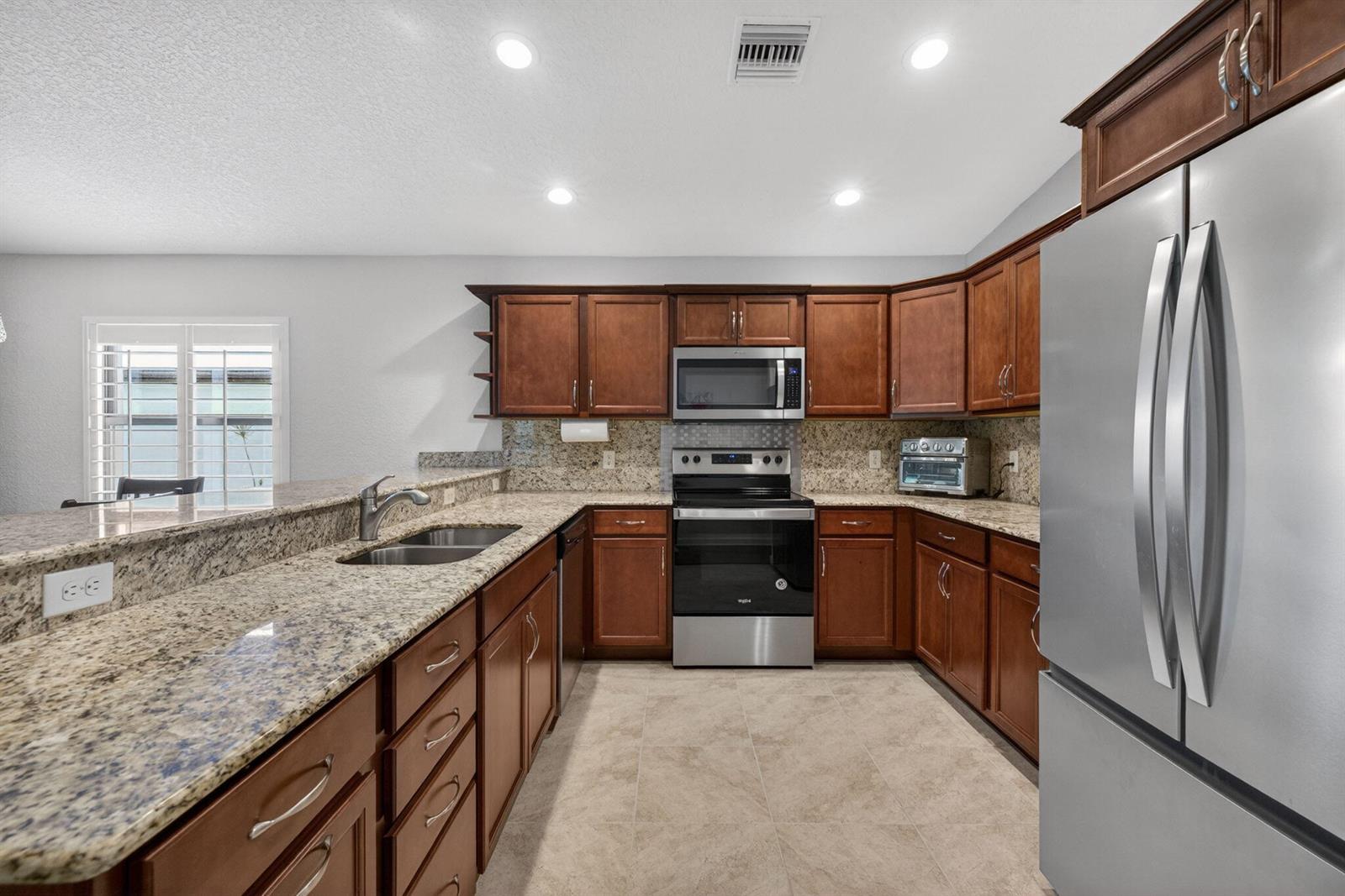 A kitchen featuring wood cabinets, granite countertops, stainless steel appliances, and tile flooring — 6456 Alemendra, Fort Pierce FL 34951, FORT PIERCE, FL