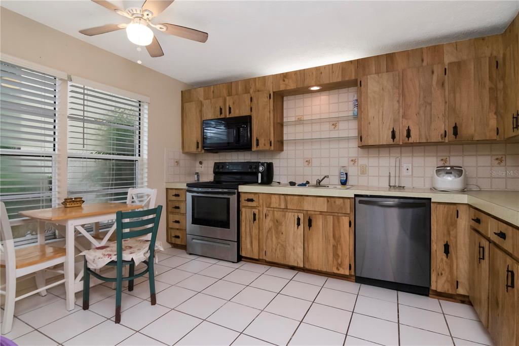 A kitchen features wood cabinets, stainless steel appliances, white tile flooring, and a small dining table — 7725 FOREST TRAIL UNIT 2, PORT RICHEY, FL