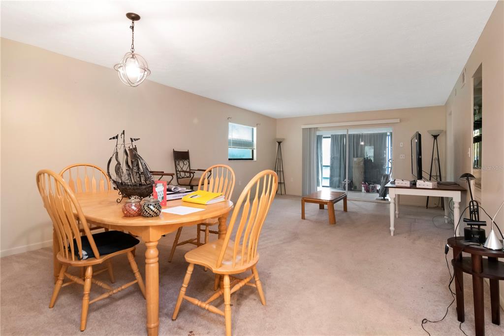 A dining area with a wooden table and chairs sits in an open carpeted living space — 7725 FOREST TRAIL UNIT 2, PORT RICHEY, FL