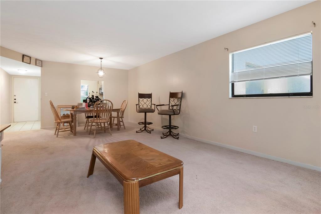 A living and dining area features beige carpeting, neutral walls, and a wooden coffee table — 7725 FOREST TRAIL UNIT 2, PORT RICHEY, FL