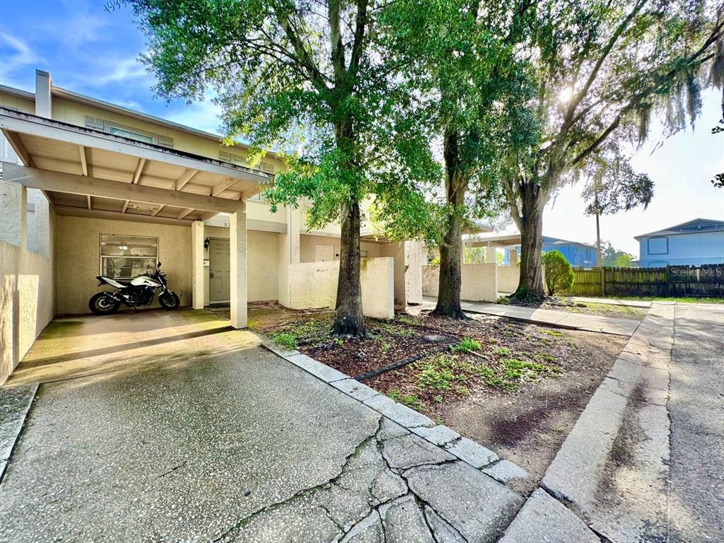 A multi-unit residential building exterior features a covered carport with a motorcycle and mature trees — 5216 TENNIS COURT CIRCLE UNIT 5216, TAMPA, FL