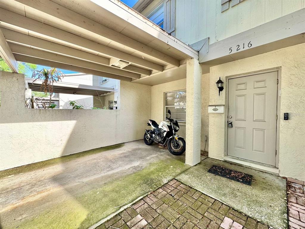 A covered carport area sits beside the front entrance of a residential building — 5216 TENNIS COURT CIRCLE UNIT 5216, TAMPA, FL