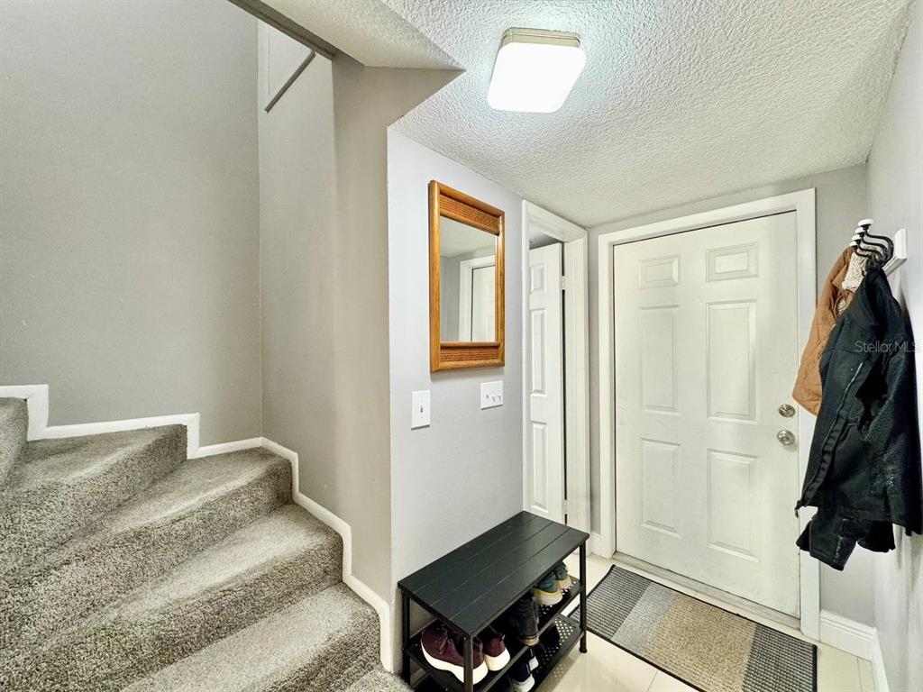 An entryway features a carpeted staircase, a black shoe rack, a mirror, and a front door — 5216 TENNIS COURT CIRCLE UNIT 5216, TAMPA, FL