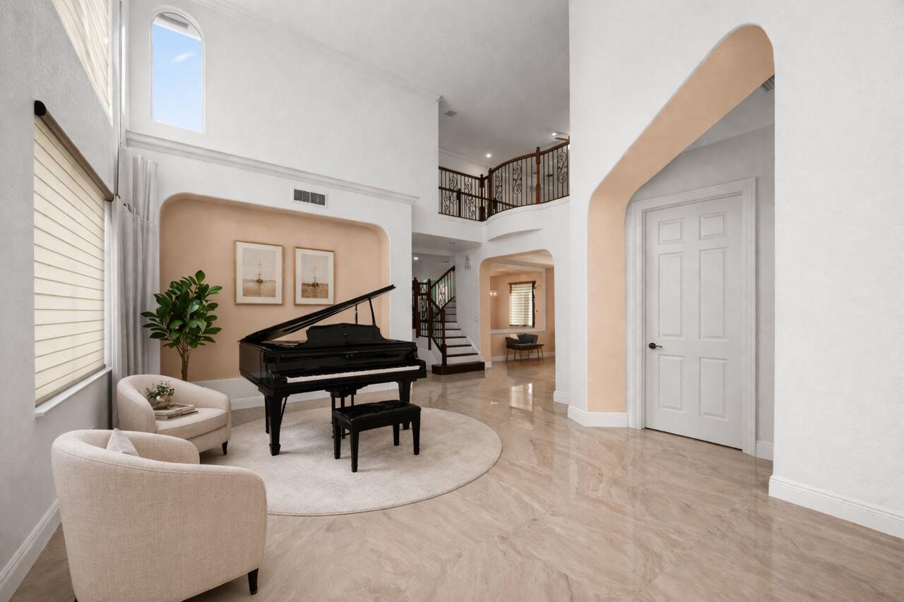 A grand foyer features a black grand piano, two armchairs, and a curved staircase — 3580 Birague Drive, Wellington FL 33449, WELLINGTON, FL