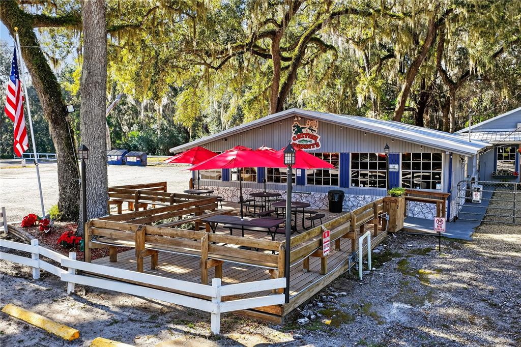 An outdoor wooden deck with tables and red umbrellas sits in front of a building — 2396 N C 470, LAKE PANASOFFKEE, FL