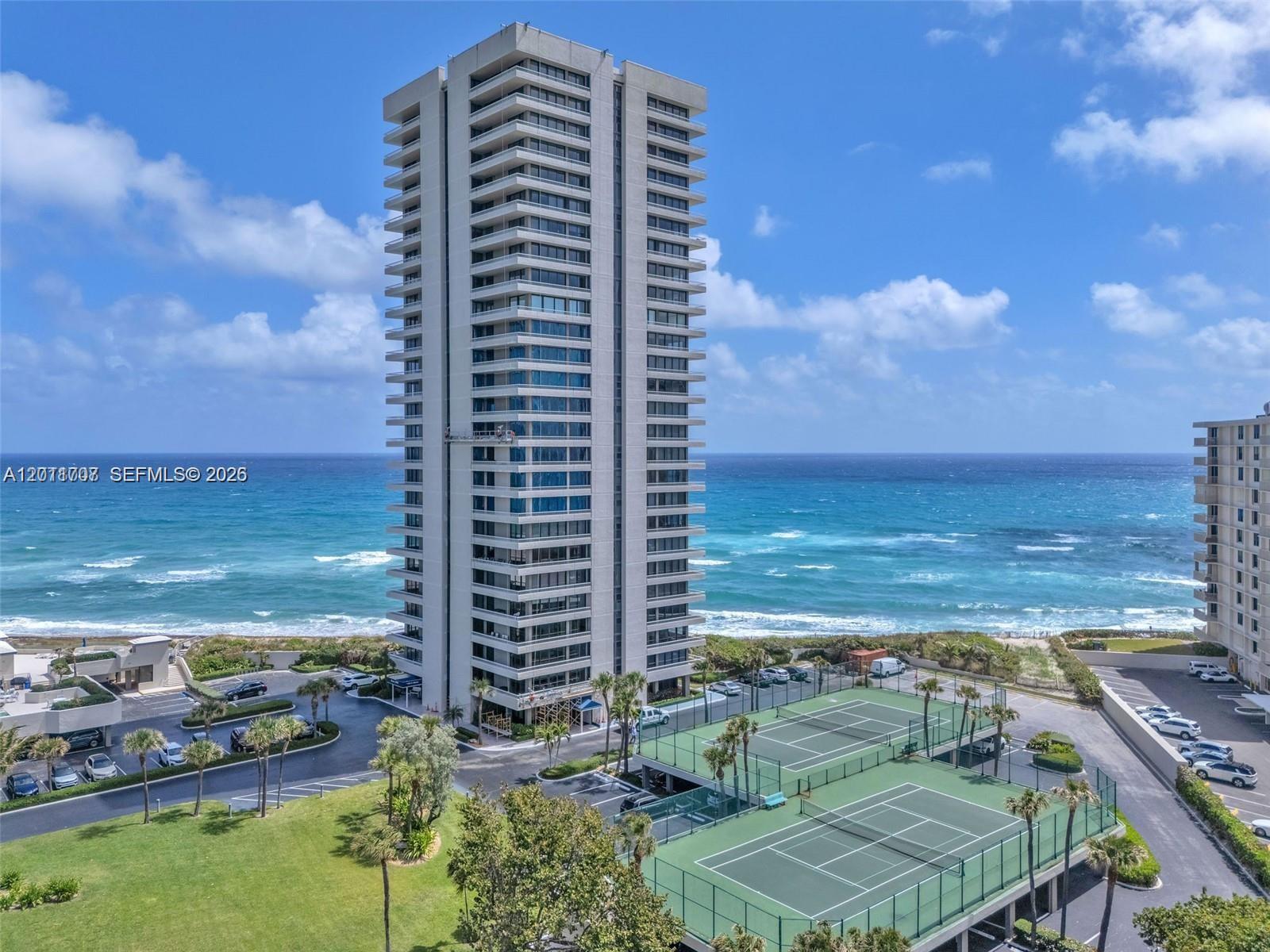 An aerial view shows a tall residential building next to tennis courts and the ocean — 5510 N Ocean Dr # 19B, Singer Island FL 33404, SINGER ISLAND, FL