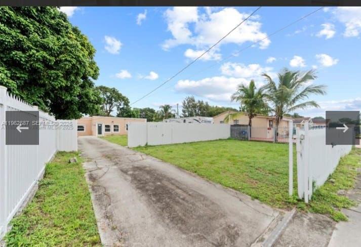 A concrete driveway leads to a single-story house behind a white fence and palm trees — 1835 NW 85th St, Miami FL 33147, MIAMI, FL