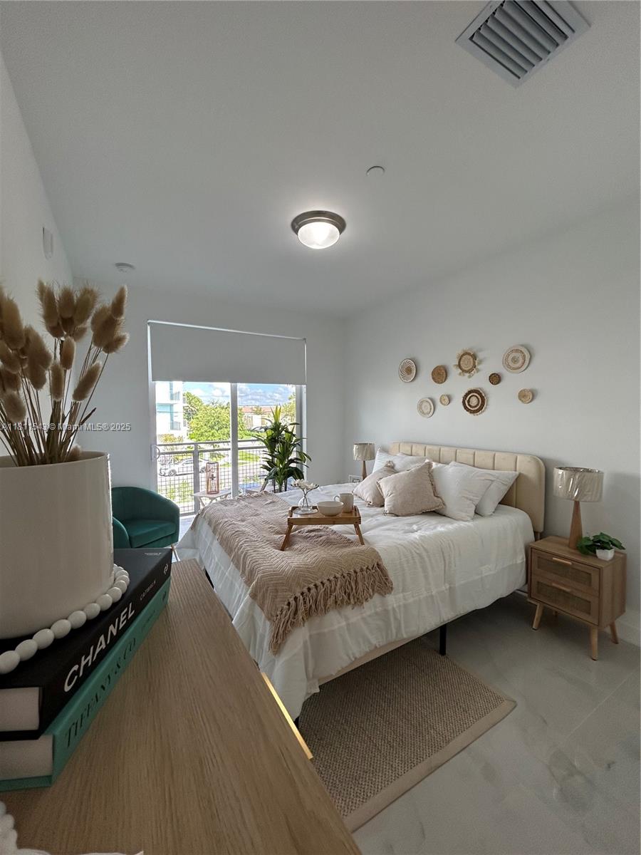 A bedroom features a bed with neutral bedding, a balcony view, and wall-mounted decorative plates — 1010 SW 69th Ave # 104, Miami FL 33144, MIAMI, FL