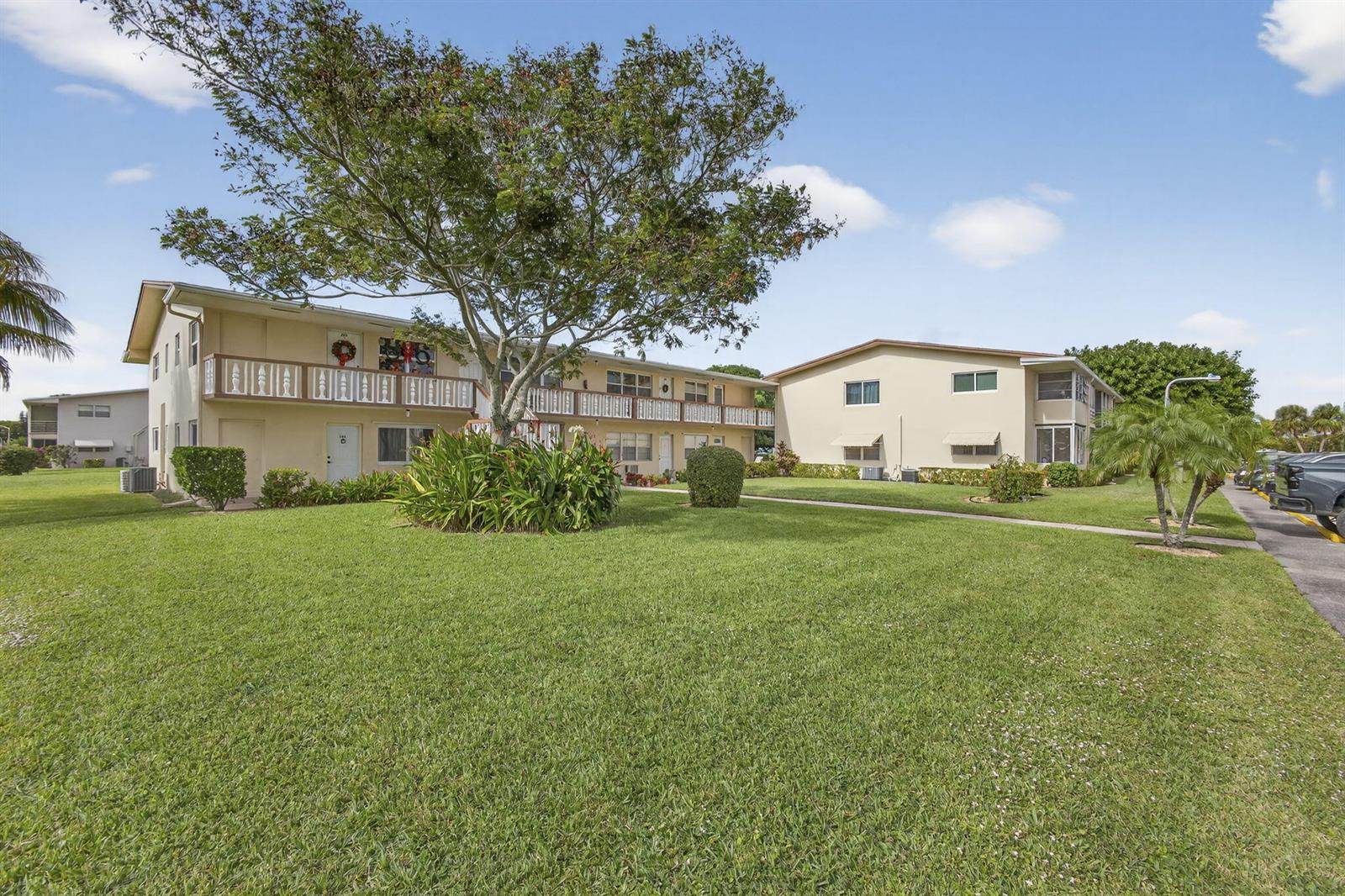 Two-story apartment buildings with balconies sit behind a large green lawn and a tree — 193 Easthampton I, West Palm Beach FL 33417, WEST PALM BEACH, FL