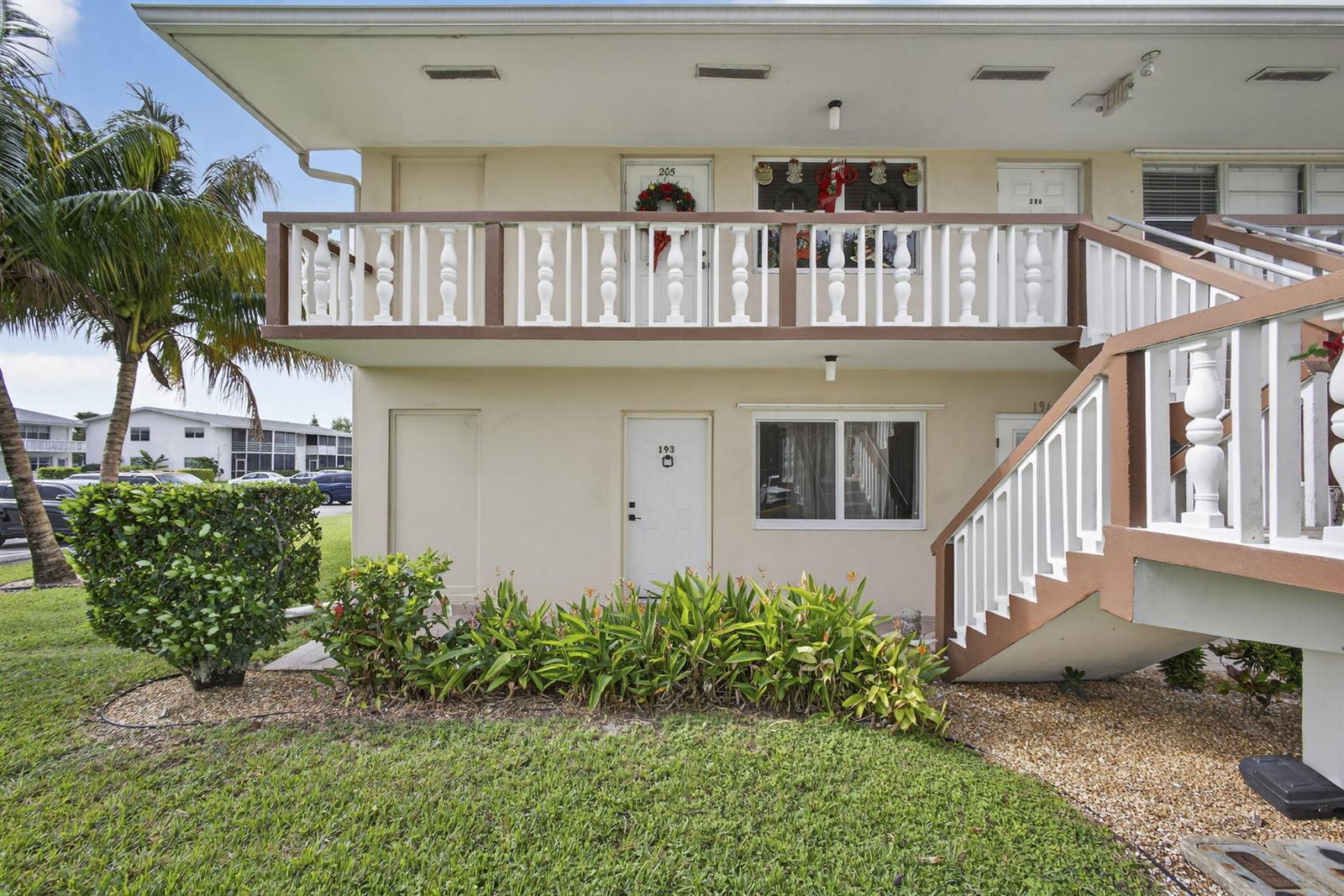 A two-story apartment building exterior features a white balcony, stairs, and ground-level unit doors — 193 Easthampton I, West Palm Beach FL 33417, WEST PALM BEACH, FL