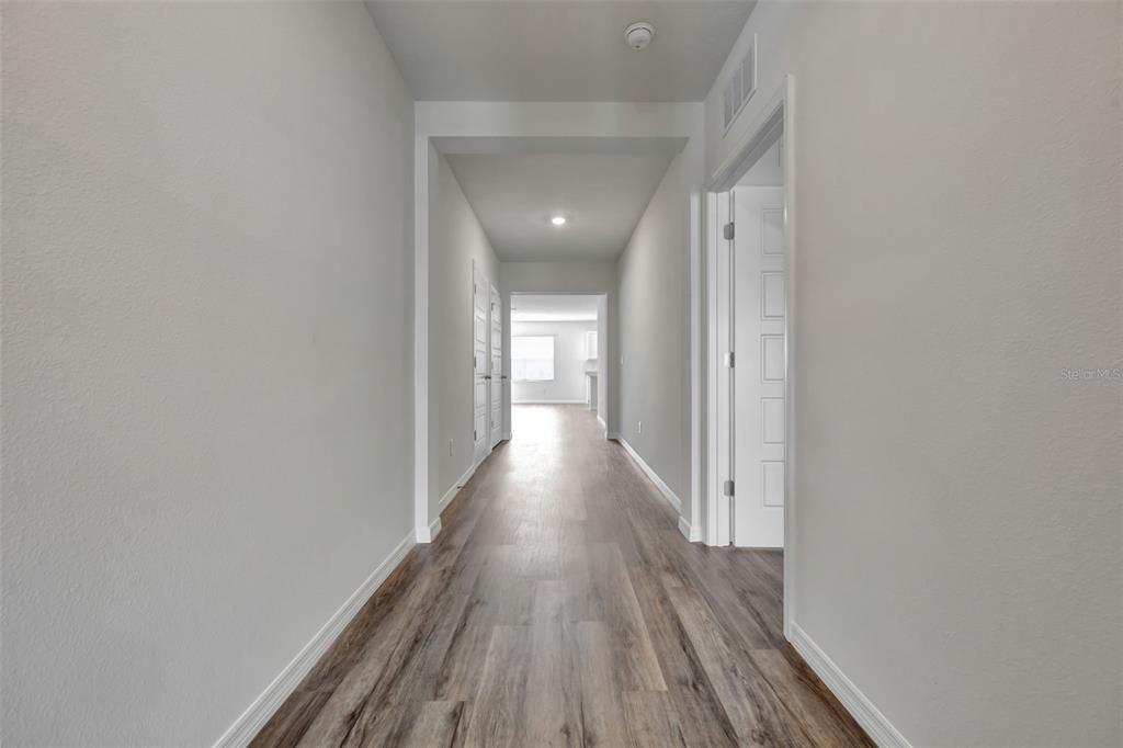 A long hallway with light gray walls and wood-look flooring leads to an open area — 3610 PFEIFFER FALLS PLACE, DAVENPORT, FL